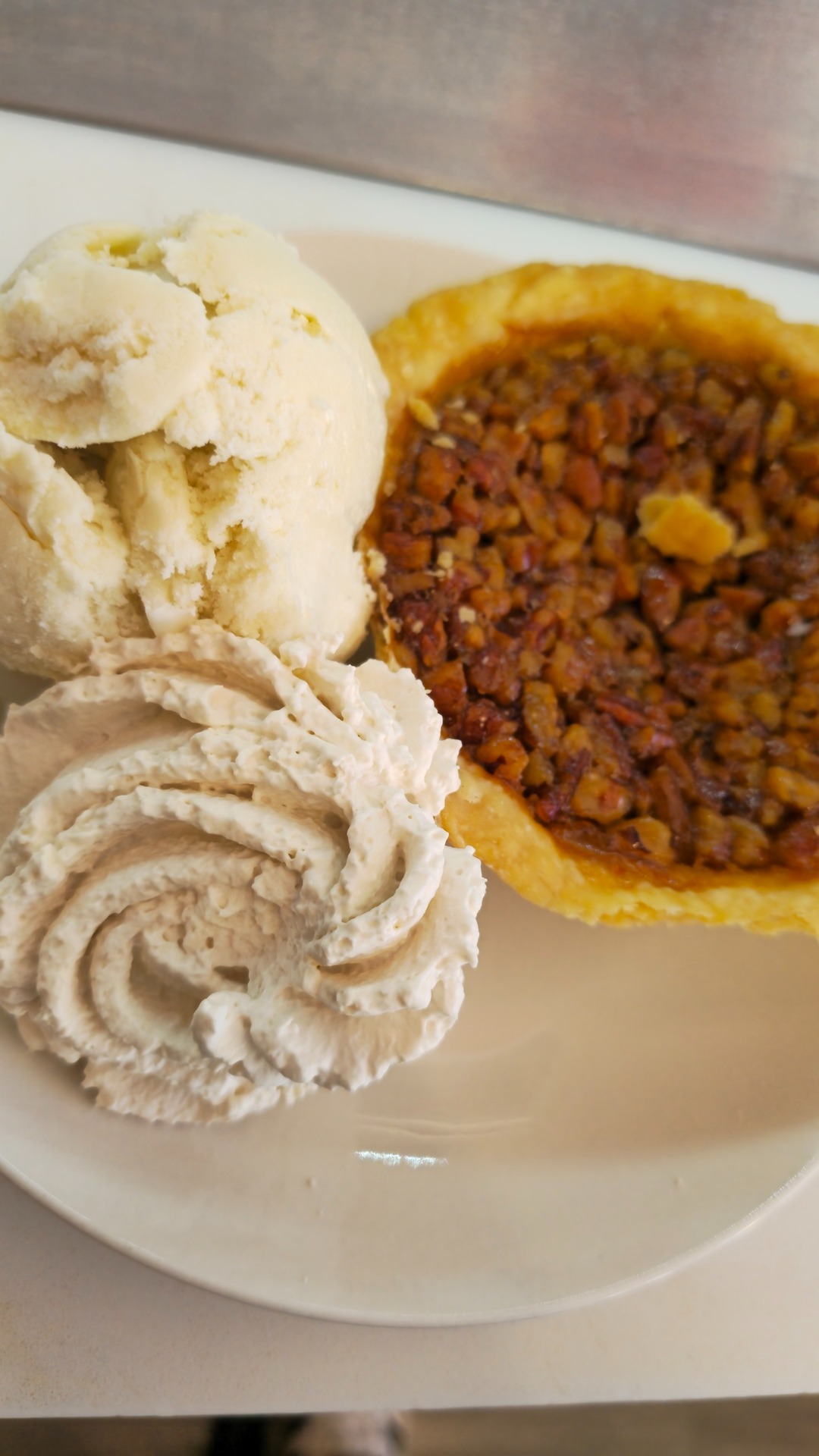 Homemade pecan pie slice served alongside vanilla ice cream scoops and cinnamon whipped cream