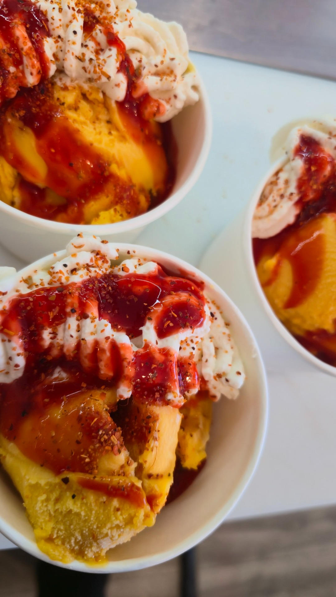 Three bowls of peach ice cream with strawberry drizzle and a dusting of cinnamon